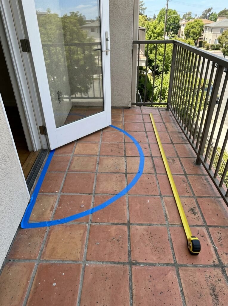 Shallow balcony floor with the outward door swing marked in tape, showing how little usable space remains