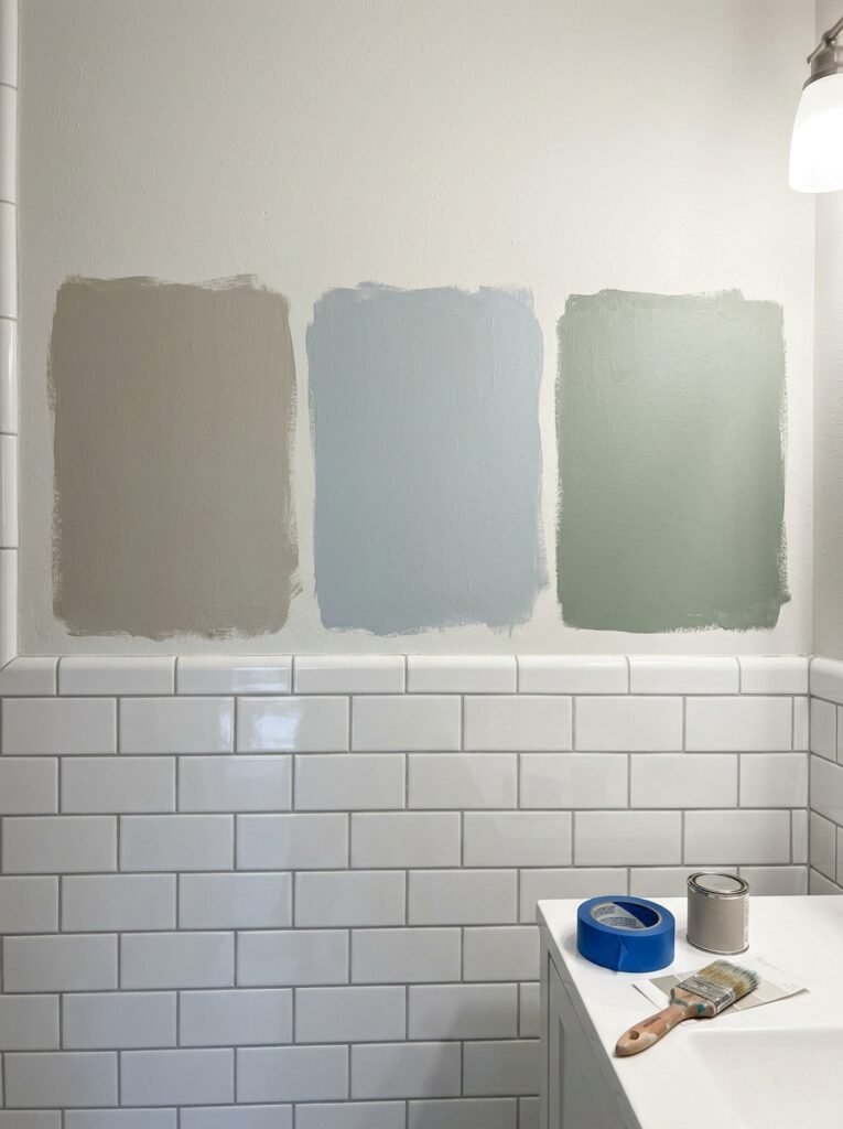  Three large painted sample patches in greige, blue-gray and sage on a bathroom wall directly above a row of white subway tile.